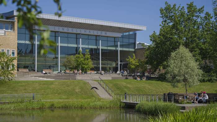Photo of a large building surrounded by trees, grass and a pond