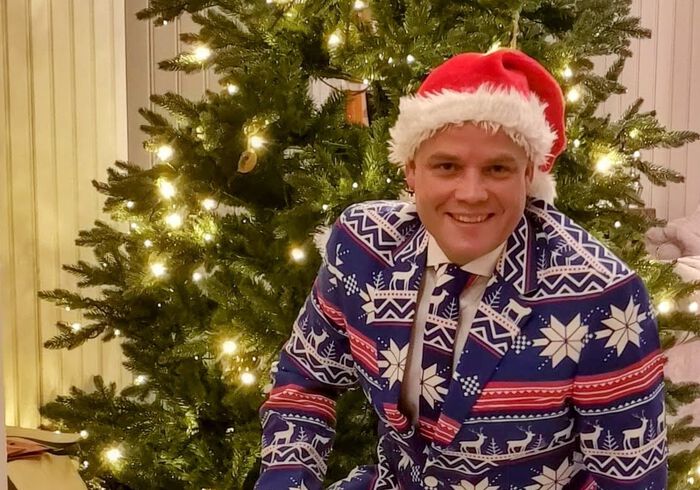 Klas foran et juletre, med en dress med julemotiv og nisselue