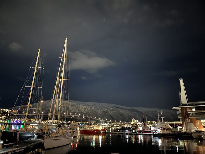 Tromsø om natten. Det er mørkt, vi ser fjorden og seilbåter som ligger til kai.