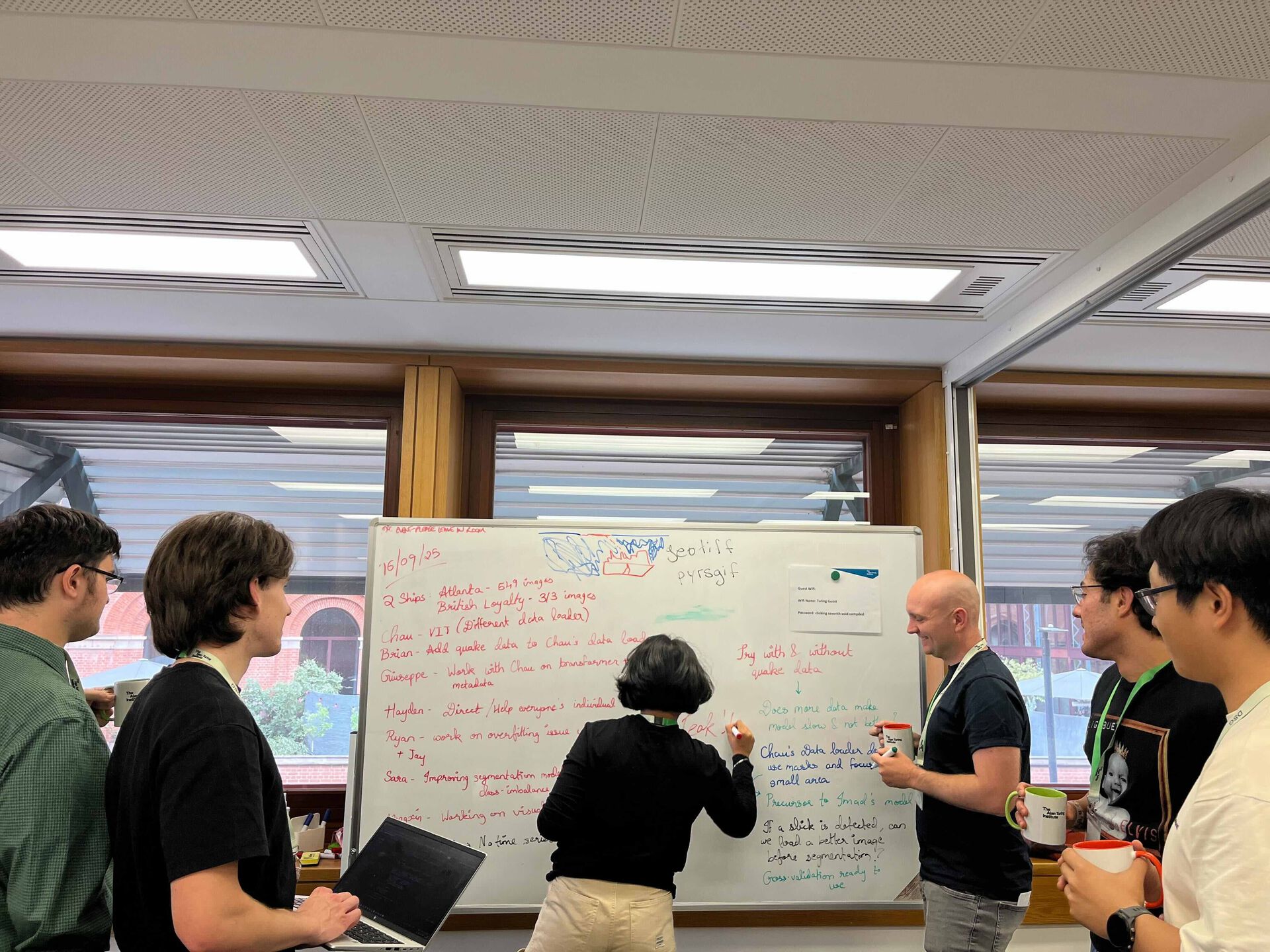 One person writing on a whiteboard, five people watching.