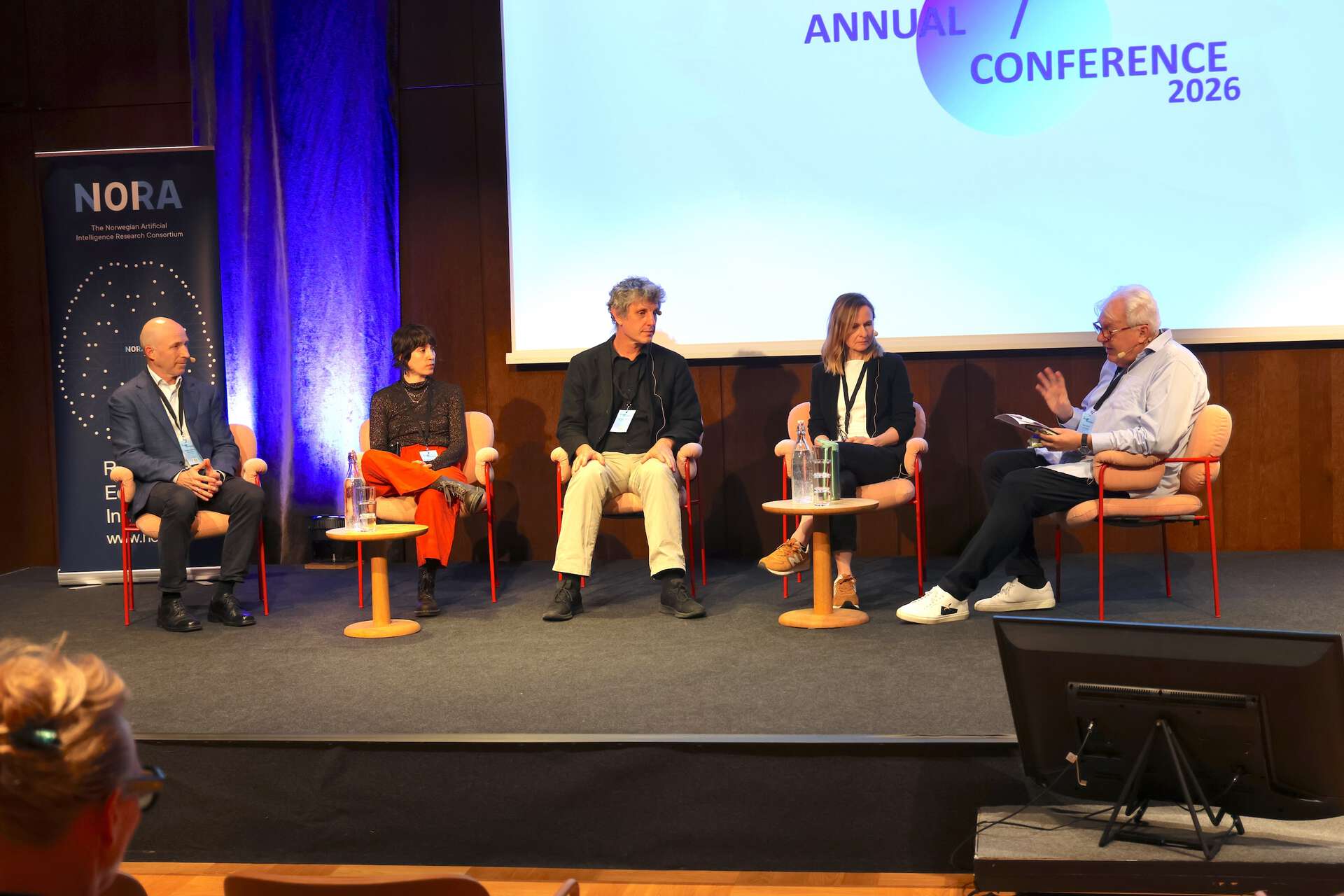 Five people sitting on stage in front of a screen