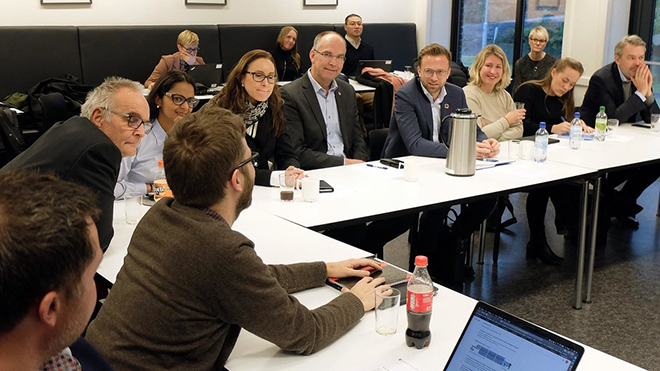 gruppe mennesker sitter rundt et bord og diskuterer