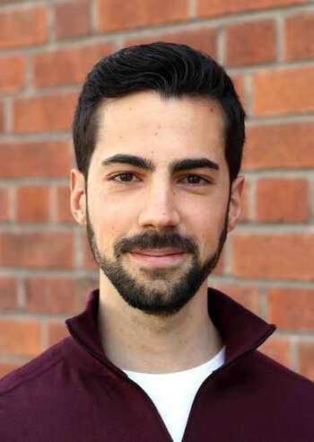 Man wearing a sweater with a zip and white t-shirt. He has a small beard.