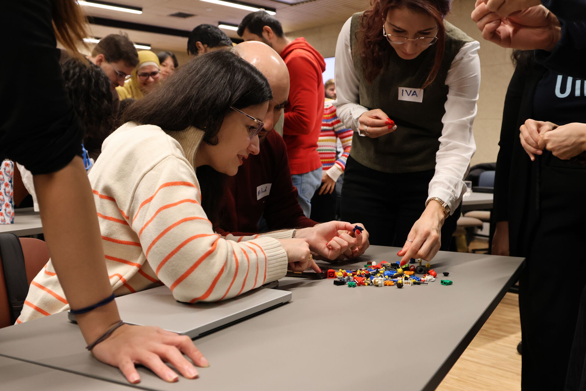 People standing around a table putting together small lego-looking pieces