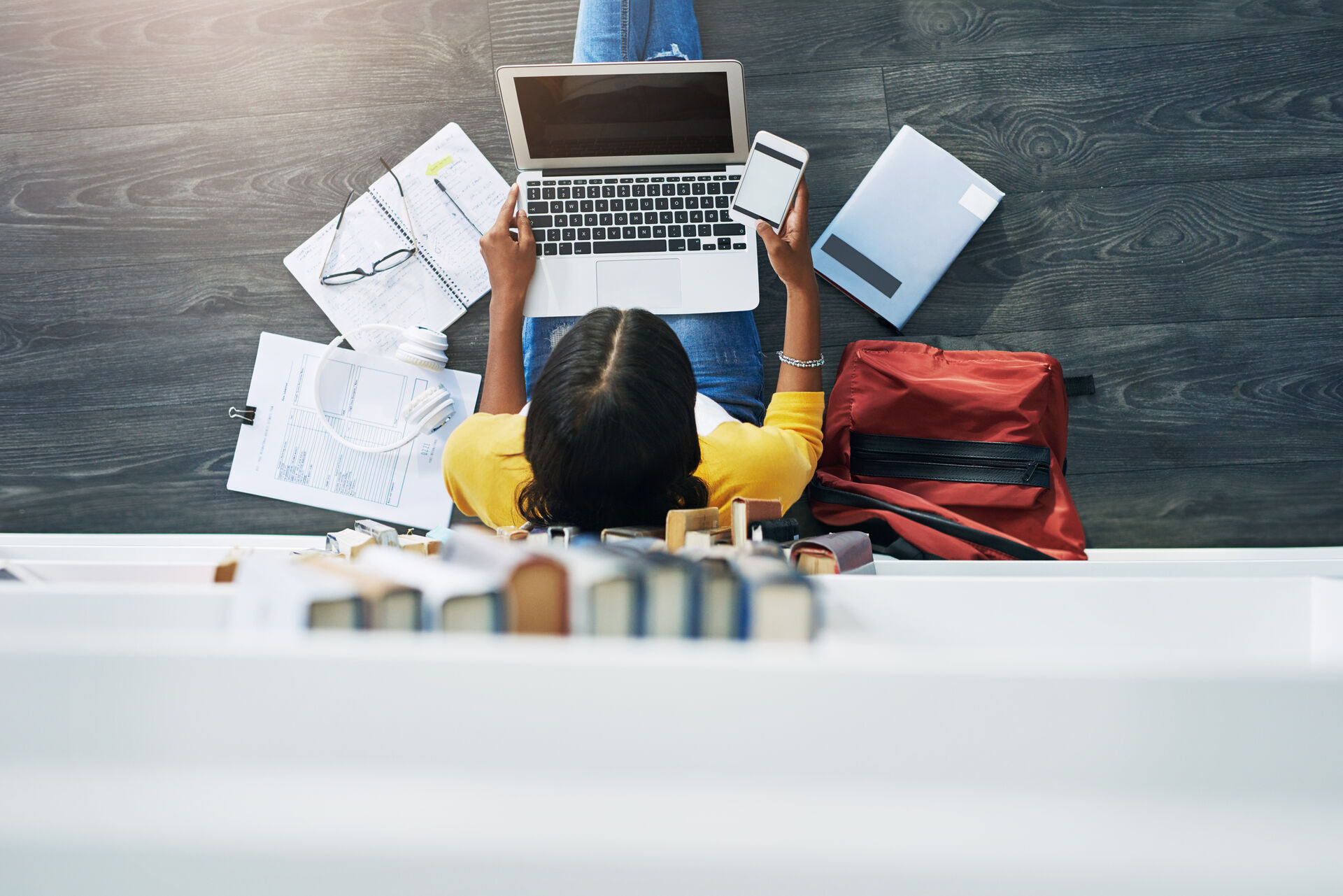 Student sitting on the floor with a laptop, documents and books.